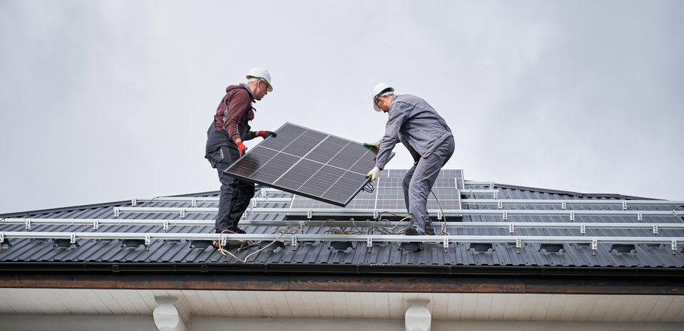 Two workers installing solar modules on the roof